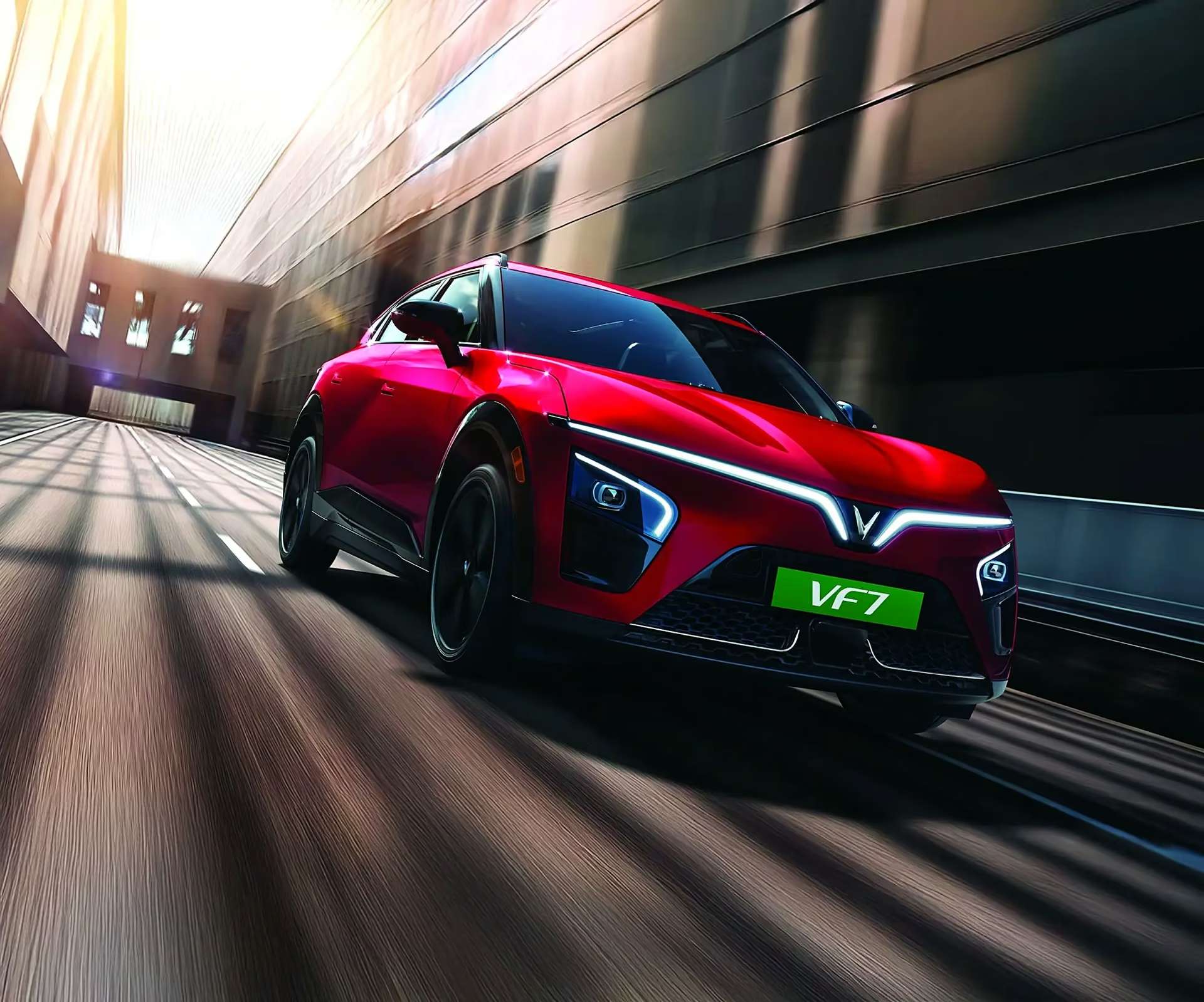 A red VinFast VF 7 driving fast through a city underpass at dusk