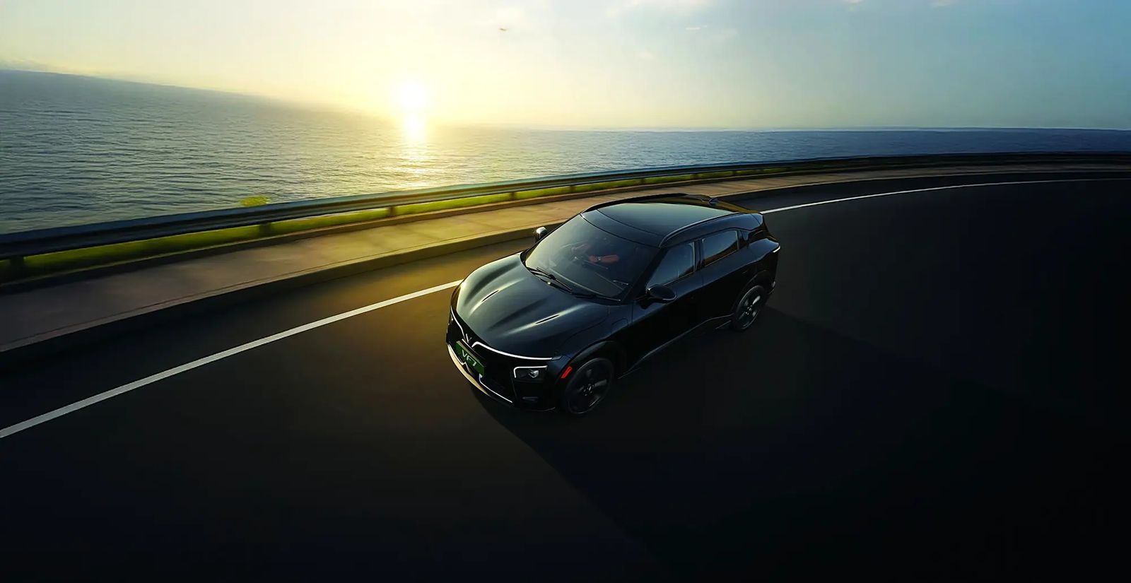 A dark VinFast VF 7 on a coastal highway at sunset